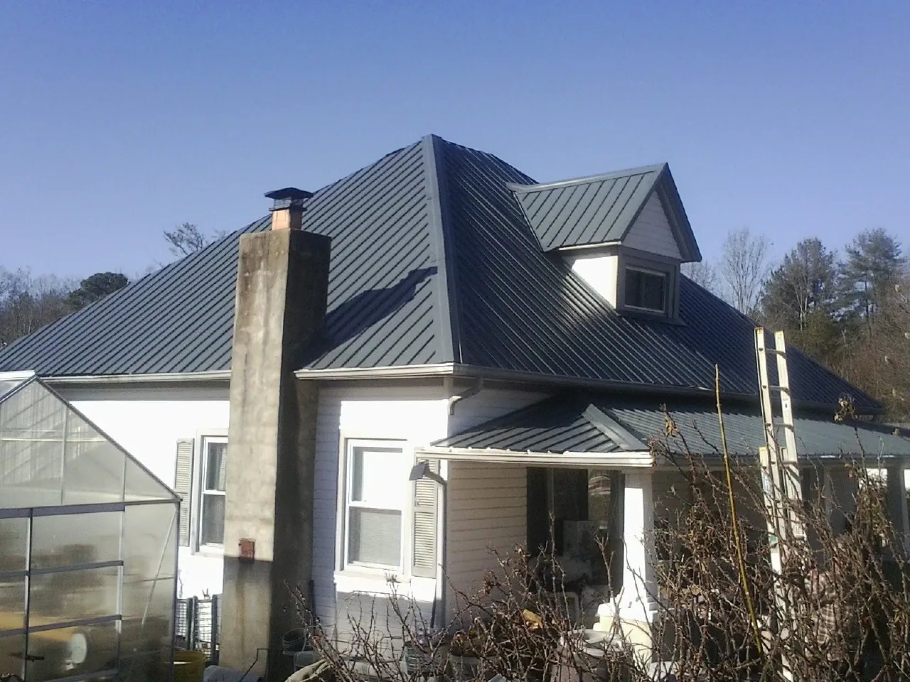 Dark blue standing seam metal roof on a white farmhouse with dormer — Slate & Tile Roof Repair by Roofing Brothers in Central Square