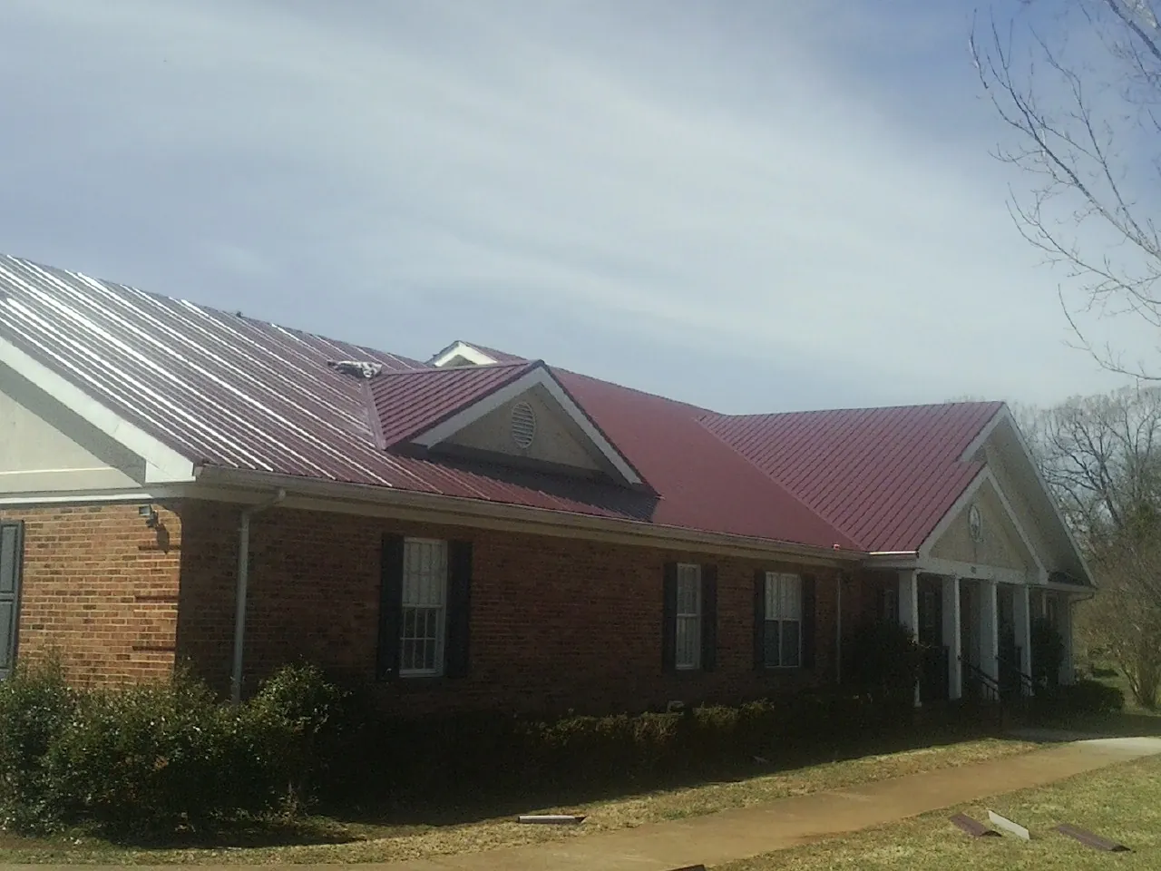 Red metal roof with gabled entries on a long brick building, from a Hail Damage Roof Repair job in Central Square