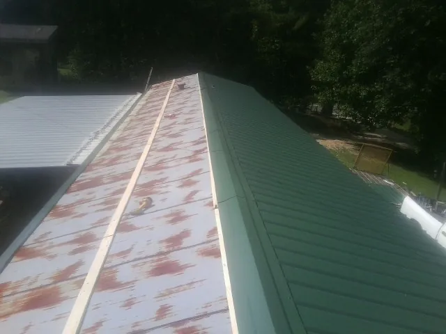 Old rusted panels beside newly installed green metal roofing — Wind Damage Roof Repair by Roofing Brothers in Central Square