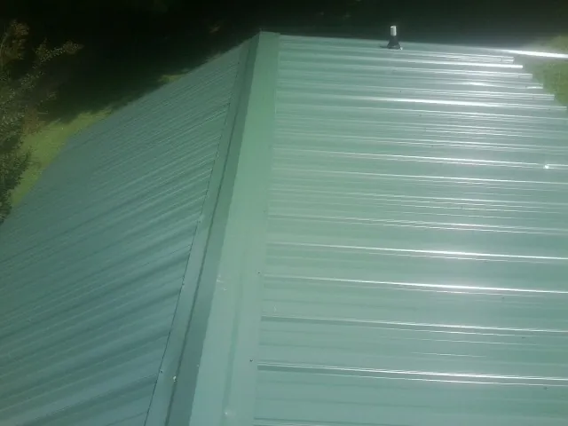 New green metal panels meeting at the ridge of a roof — Flat Roof Repair work by our crew in Central Square