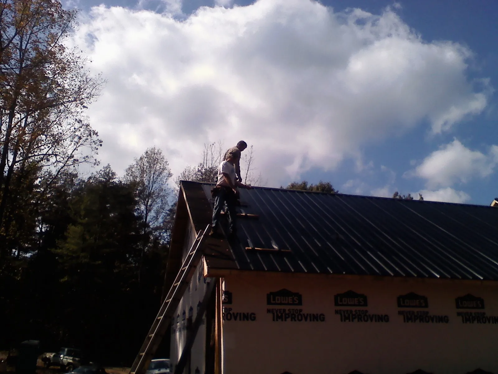 Roofer fastening dark metal panels high against a cloudy sky, from a Roof Inspection job in Central Square